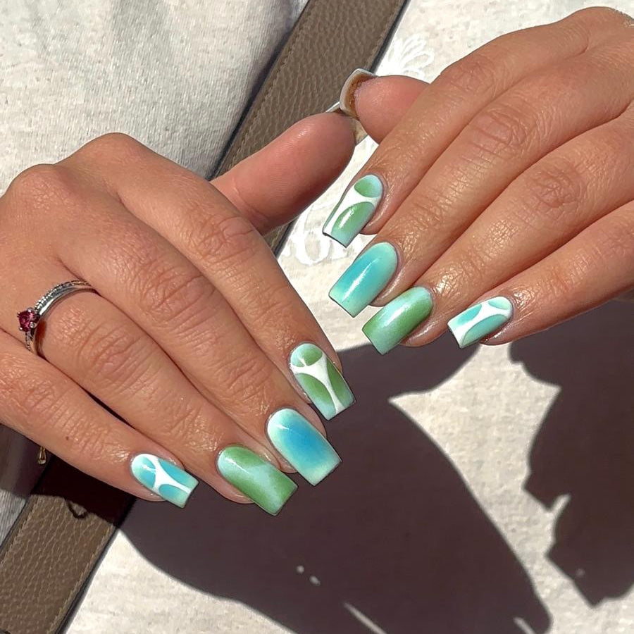 Close-up of hands with turquoise and green nail polish on a gray background