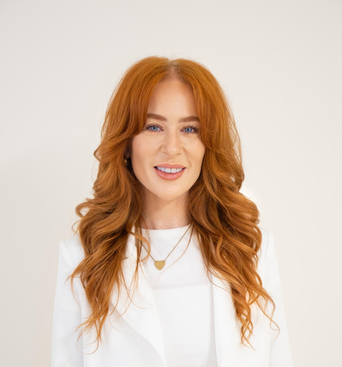 Woman with long wavy red hair wearing a white top against a light background