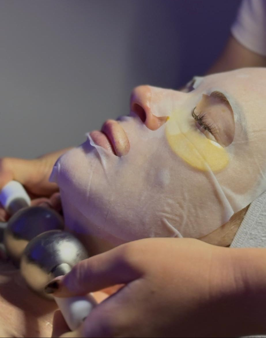 Person receiving a facial treatment with a mask on a neutral background