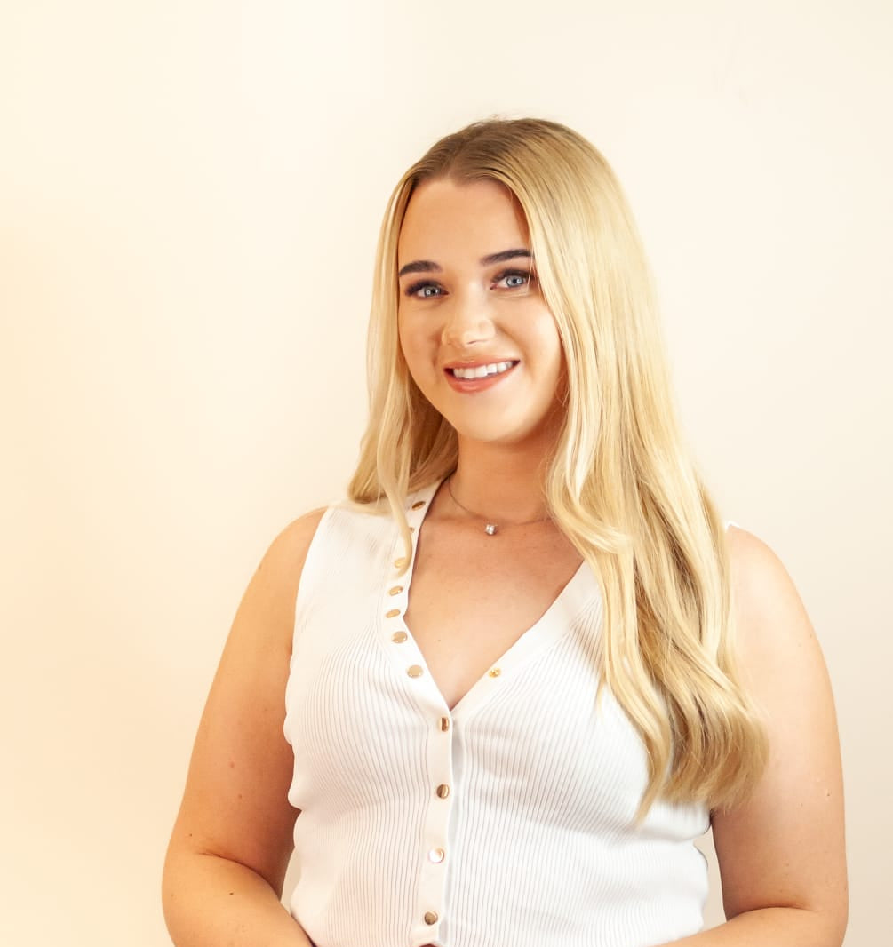Woman wearing a white sleeveless top with buttons and blue jeans against a beige background